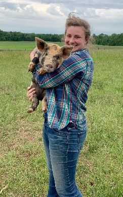 Sarah Campbell, the National Beginning Farmer and Rancher Program Coordinator based in Washington, D.C., holding a pig and smiling in a green pasture.