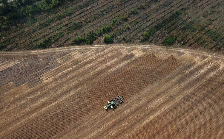 A birds eye view of a tractor plowing a large farm field.