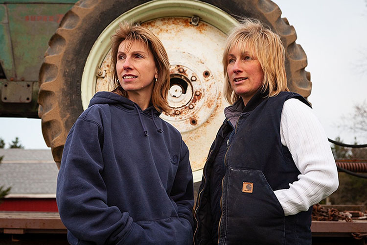 A photo of Nina and Kim standing in front of heavy-duty farm equipment.