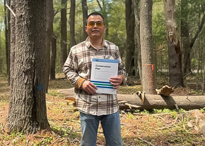 Shimin Liu, wearing a plat shirt and blue jeans, holds a conservation plan