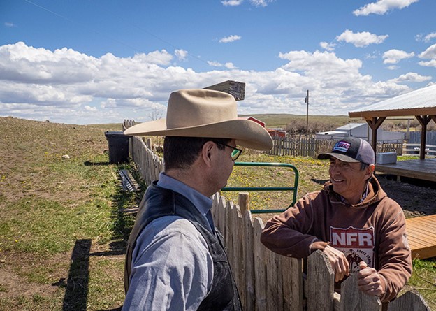 Two people talking while leaning on wooden fence
