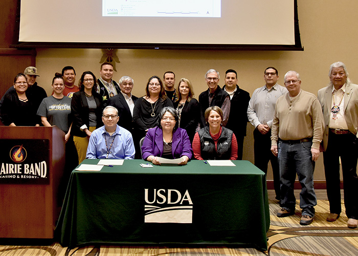 Eighteen people standing behind podium smiling