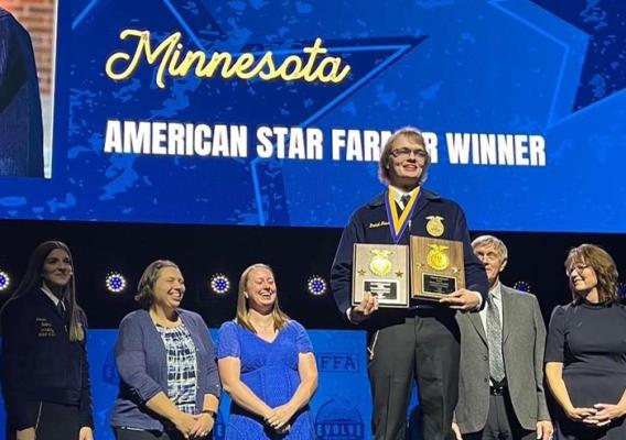 Person posing with plaques in hand on a stage