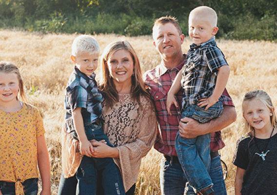 A mother, father, and four children stand in a field